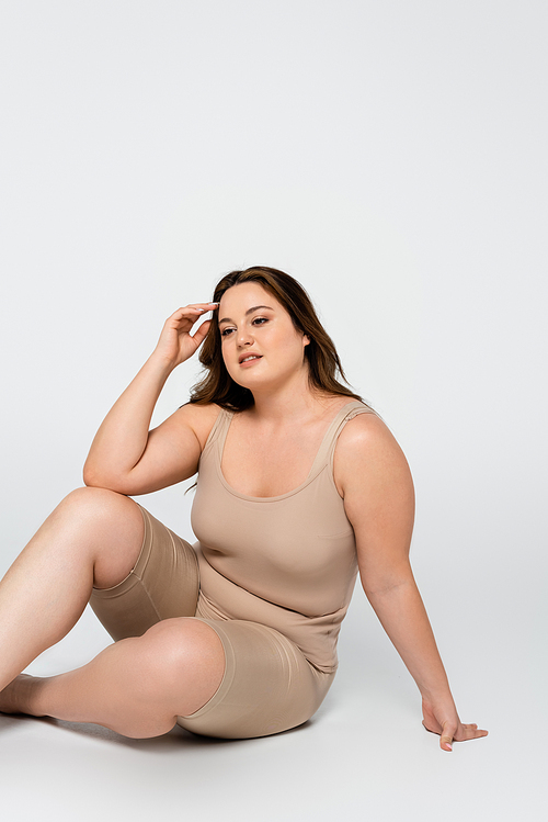 Smiling body positive woman sitting on grey background