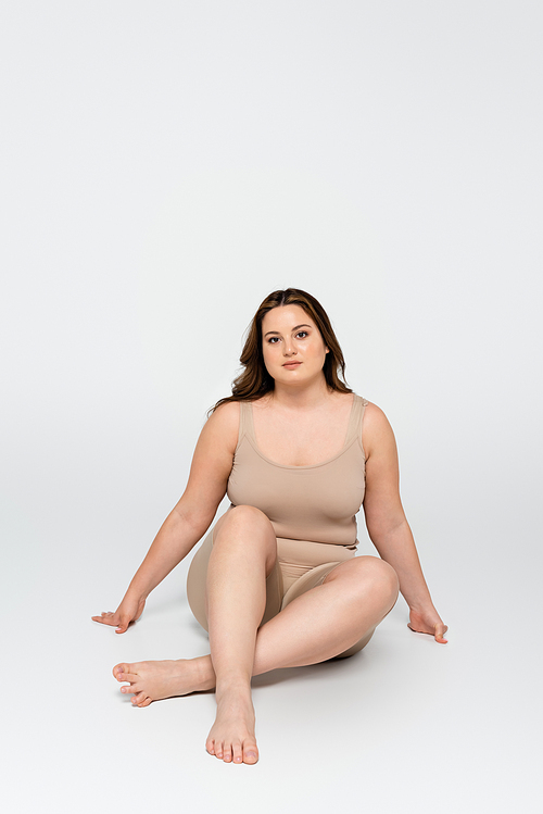 Barefoot body positive woman  while sitting on grey background