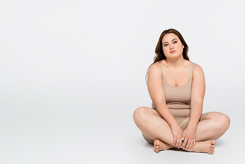Brunette woman with overweight sitting with crossed legs on grey background