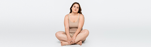 Pretty body positive woman crossing legs while sitting on grey background, banner