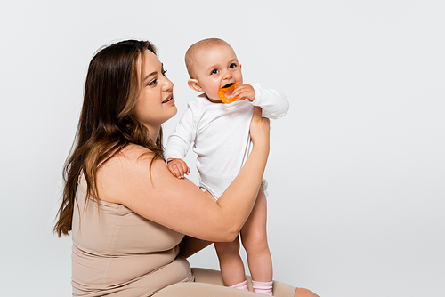 Brunette mother with overweight holding baby with toy isolated on grey