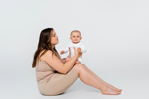 Young woman with overweight holding child while sitting on grey background
