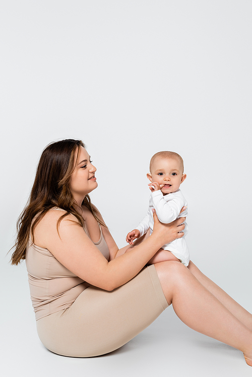 Pretty plus size woman holding child with finger near mouth on grey background