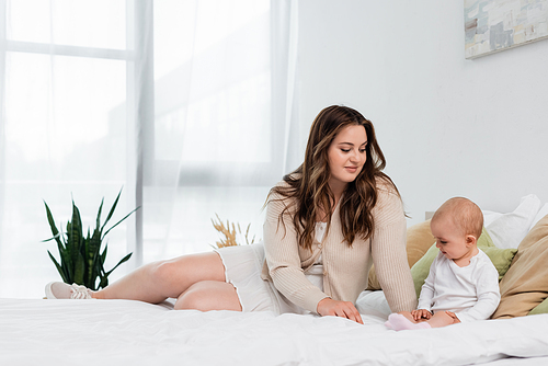 Smiling plus size woman looking at baby daughter on bed