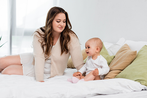 Happy plus size mother looking at smiling child on bed in bedroom