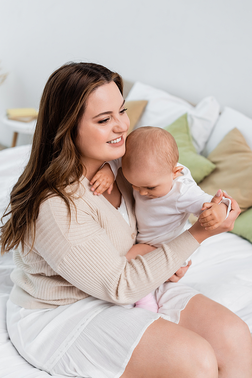 Happy plus size mother hugging baby girl on bed at home