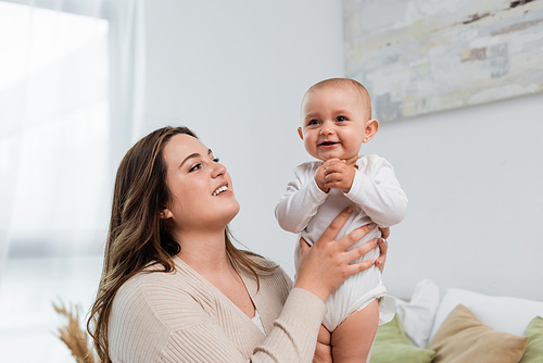 Young plus size woman holding smiling baby daughter at home