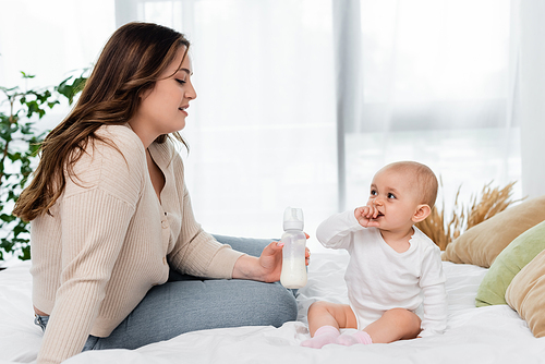Plus size mother holding bottle of milk near daughter on bed