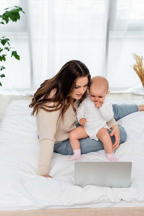 Woman with overweight holding baby daughter near laptop on bed