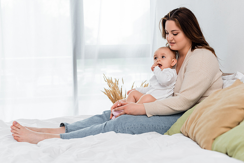 Positive body positive mother touching legs of baby daughter on bed