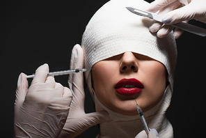 woman in elastic bandage near plastic surgeons with surgical knife and syringes isolated on grey