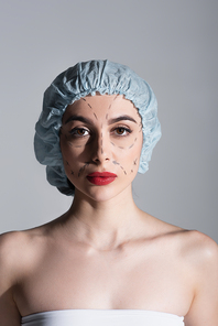 young woman in surgical cap with marked lines on face isolated on grey