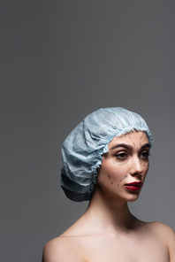 young woman in surgical cap with marked lines on face looking away isolated on dark grey