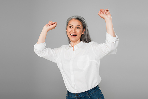excited middle aged woman in white blouse showing rejoice gesture isolated on grey