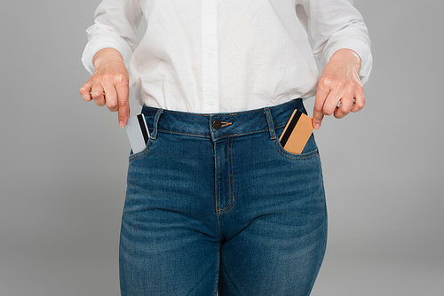 partial view of woman taking credit cards from pockets of blue jeans isolated on grey