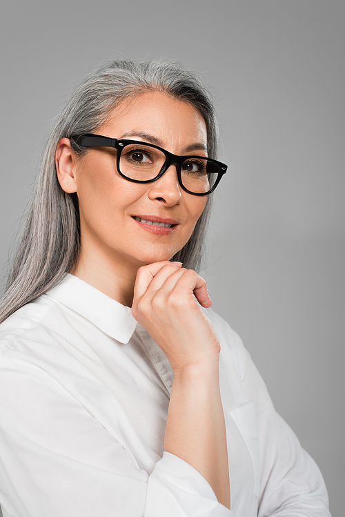 middle aged woman in stylish eyeglasses smiling at camera isolated on grey