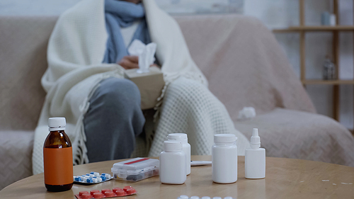 cropped view of blurred sick man sitting near medicaments on table