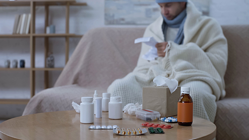 selective focus of medicaments on table near sick man reading medication instruction on blurred background