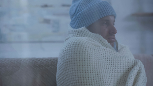sick man in warm hat and blanket sitting on couch at home