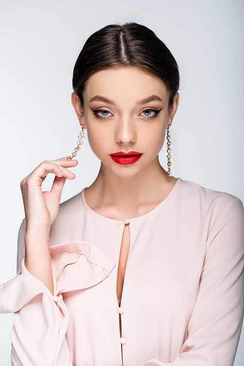 pretty woman with red lips  while touching earring isolated on grey