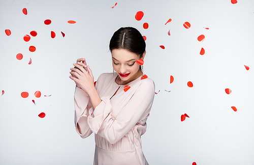 young and happy woman near falling rose petals on grey