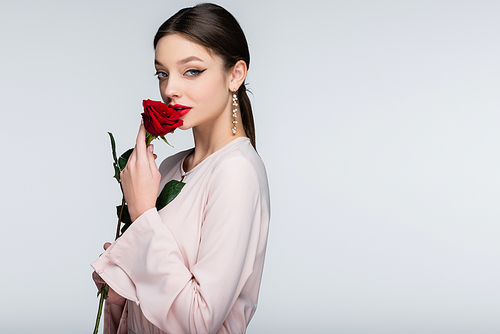brunette young woman with red lips smelling rose isolated on grey