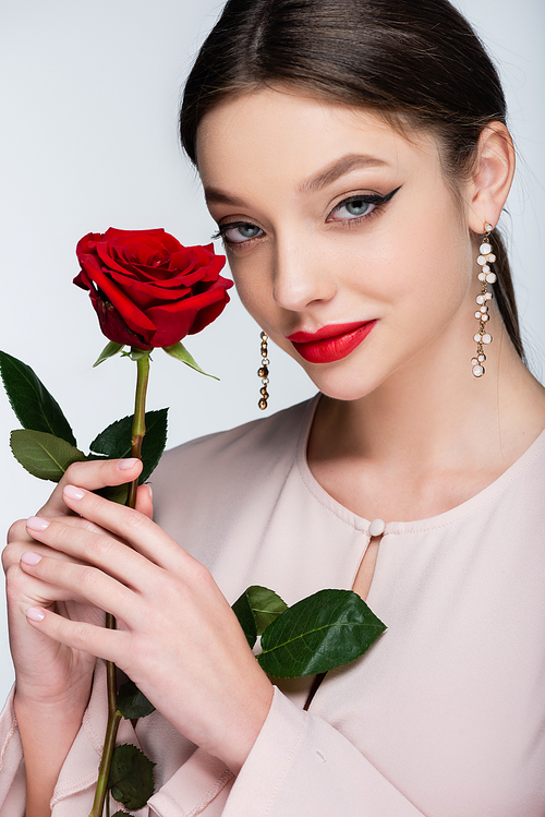 pretty young woman in earrings and blouse holding red rose isolated on grey