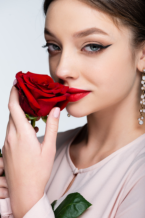 brunette woman with red lips smelling rose isolated on grey