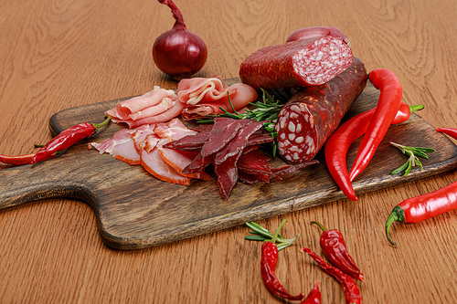 delicious meat platter served with chili pepper and rosemary on wooden table