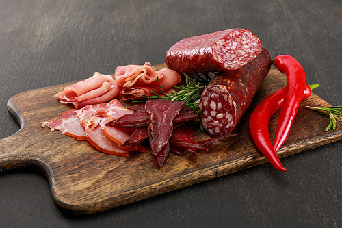 delicious meat platter served with chili pepper and rosemary on wooden black table