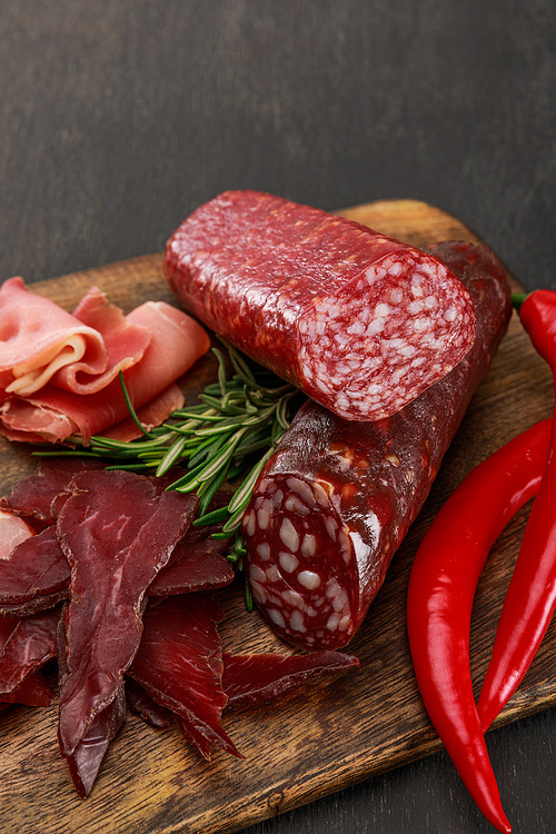 close up view of delicious meat platter served with chili pepper and rosemary on wooden black table