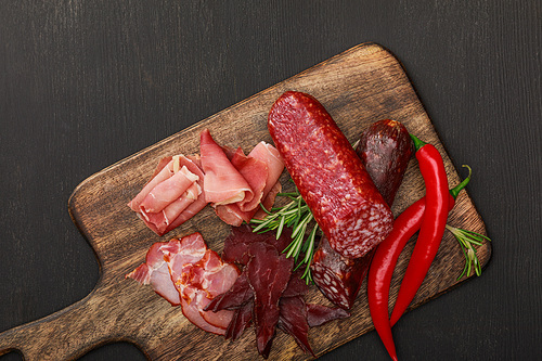 top view of delicious meat platter served with chili pepper and rosemary on wooden black table