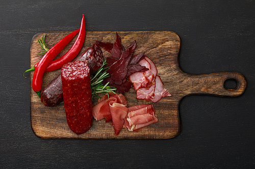 top view of delicious meat platter served with chili pepper and rosemary on wooden black table