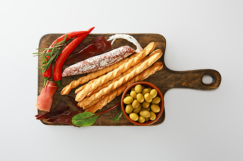 top view of delicious meat platter served with breadsticks, olives, chili peppers and herbs on board isolated on white