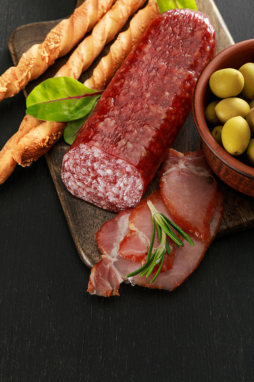 delicious meat platter served with olives and grissini on board on black surface