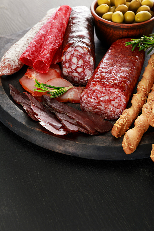 tasty meat platter served with olives and grissini on board on black surface