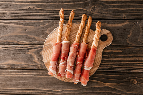 top view of delicious meat platter with breadsticks and prosciutto on wooden board