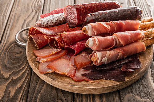 top view of delicious meat platter served with breadsticks on wooden board