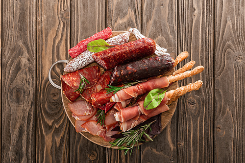 top view of delicious meat platter served with rosemary and breadsticks on wooden board