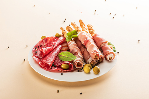 delicious meat platter served with olives and breadsticks on plate on beige