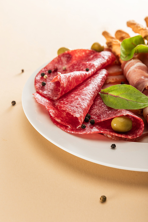 close up view of delicious meat platter served with olives and breadsticks on plate on beige