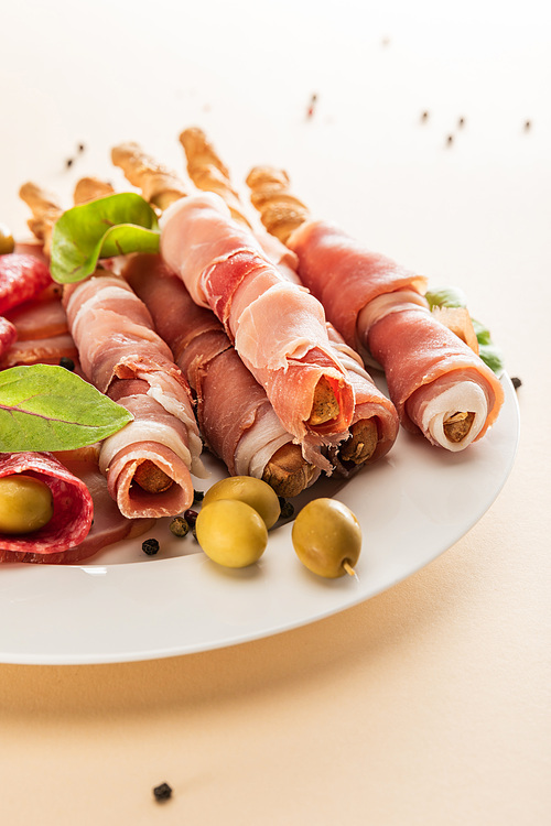 delicious meat platter served with olives and breadsticks on plate on beige