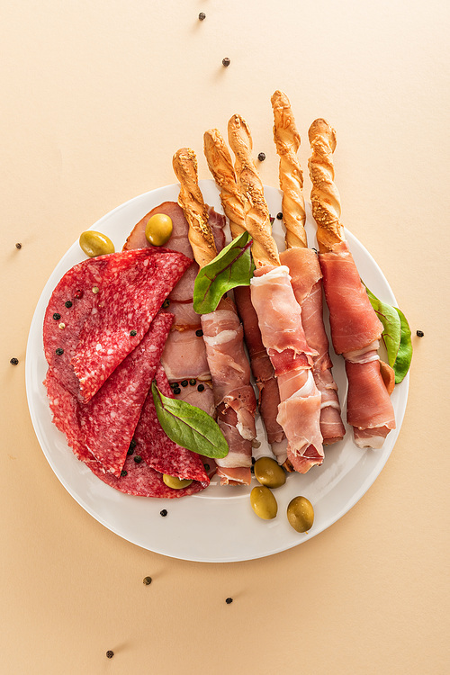 top view of delicious meat platter served with olives and breadsticks on plate on beige