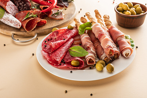delicious meat platters served with olives, spices and breadsticks on plate and wooden board on beige