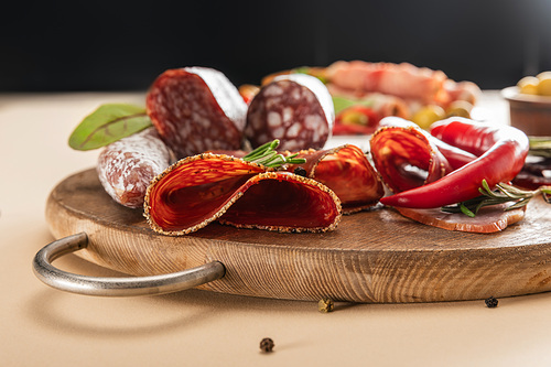 delicious meat platters served with rosemary and chili pepper on wooden board on beige