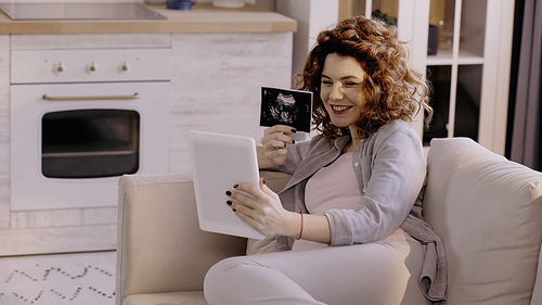 Happy pregnant woman with ultrasound scan of baby having video call on digital tablet at home