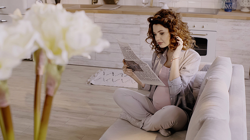 Pregnant woman reading newspaper on couch at home