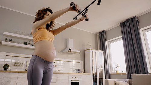 Low angle view of pregnant woman training with dumbbells at home