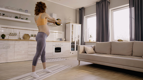 Pregnant woman working out with slam ball on fitness mat at home