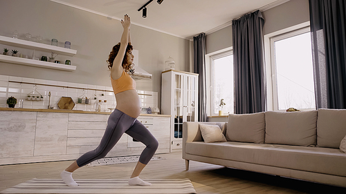 Side view of pregnant woman training on fitness mat near couch at home